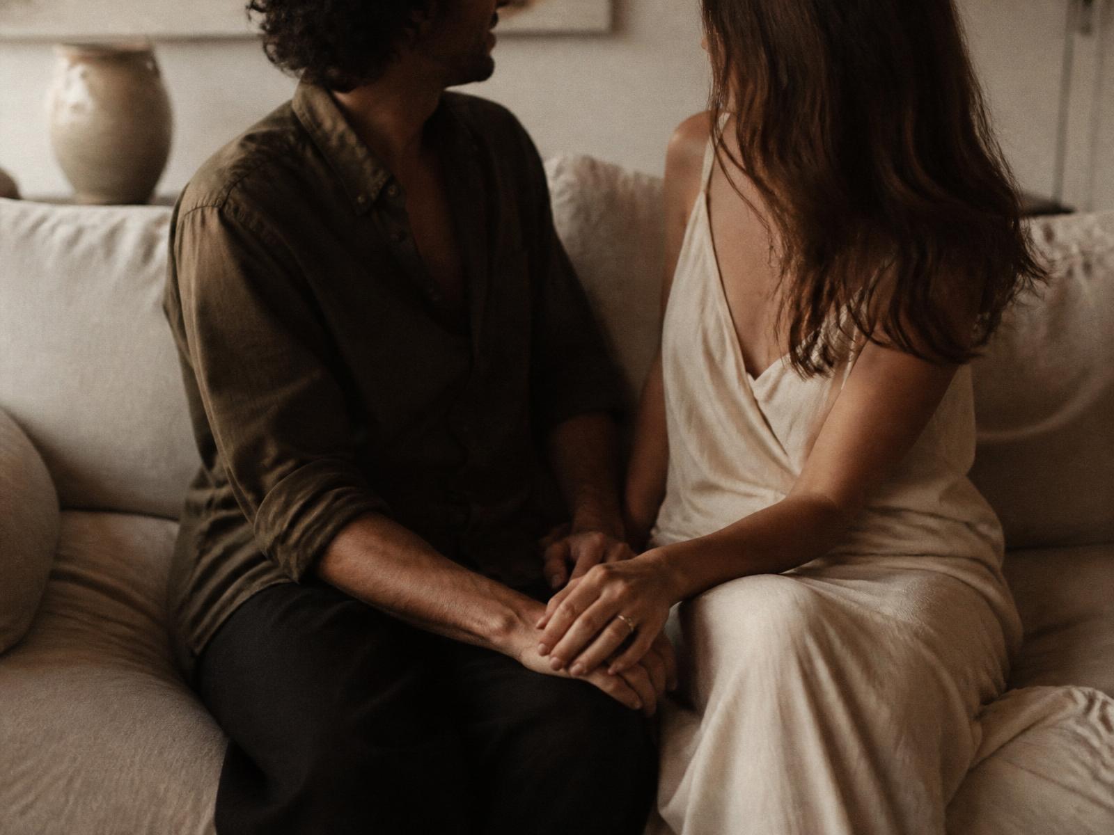 A couple sitting close on a couch, hands resting together
