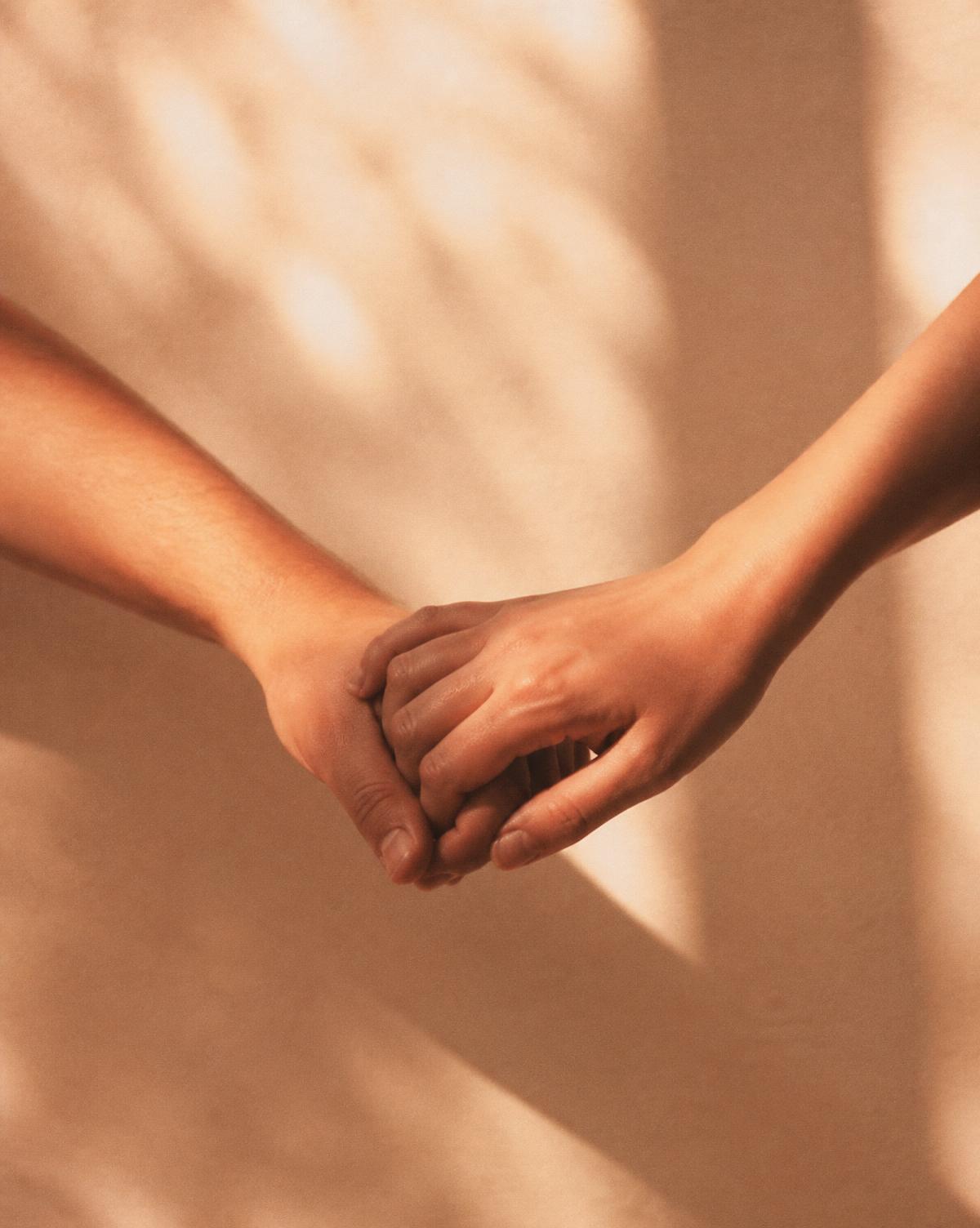 Two hands clasped in warm light — Relationship Intensives with Karem Muksed
